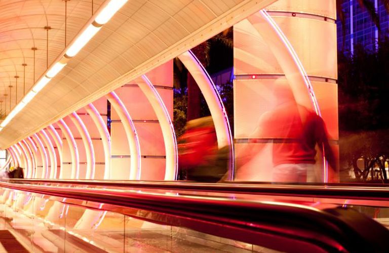 Lenvi image of a white and pink tunnel with a moving walkway and blurred figures